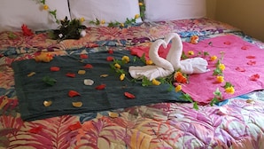 Een bed met een bloemenbedekking, witte kussens en een decoratieve zwaan als handdoek.