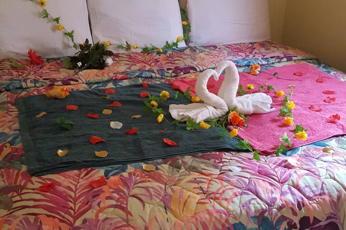 Una cama con colcha floral, almohadas blancas y una toalla decorativa con forma de cisne.