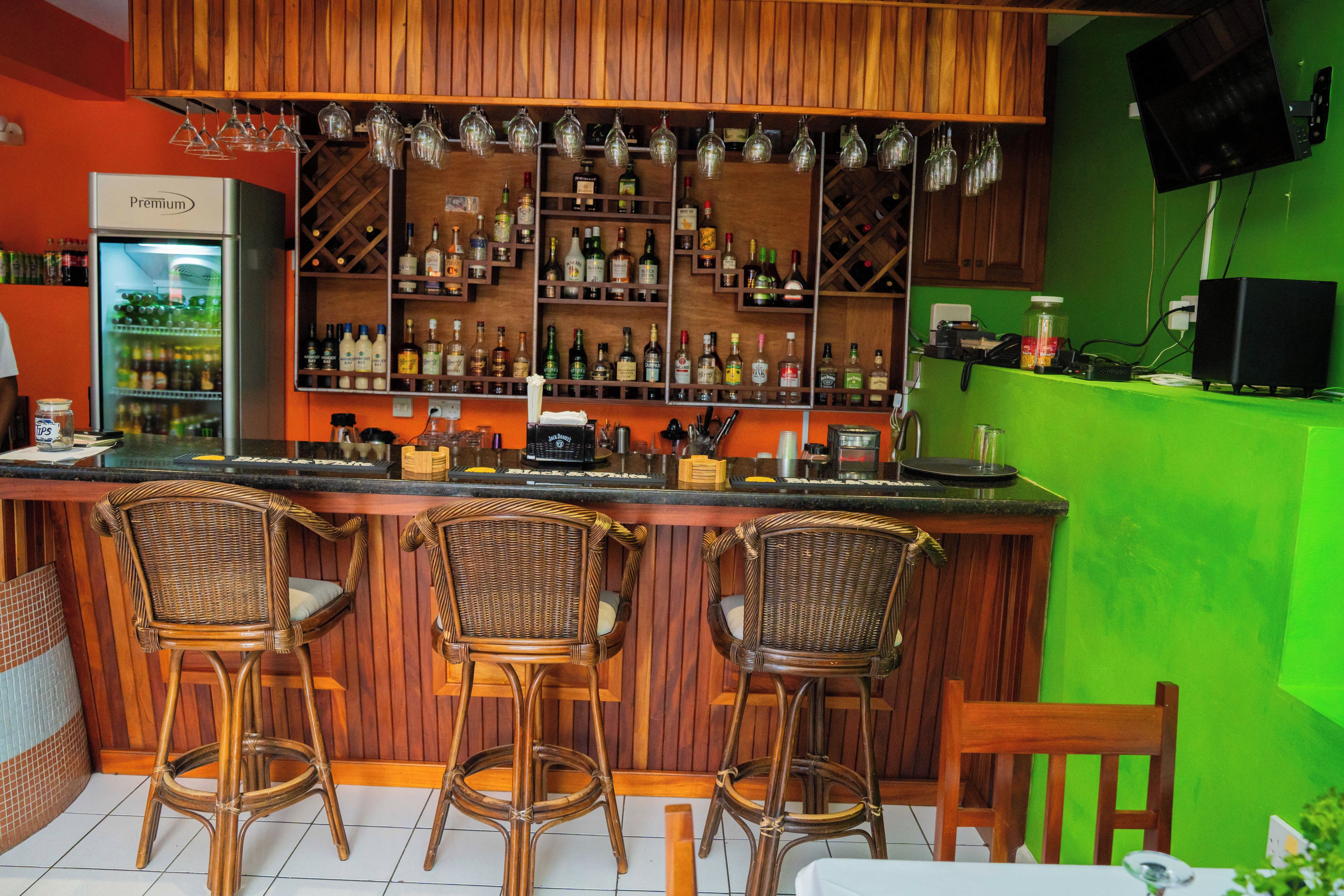A bar area with wooden shelves stocked with bottles, a refrigerator, and three wicker bar stools.