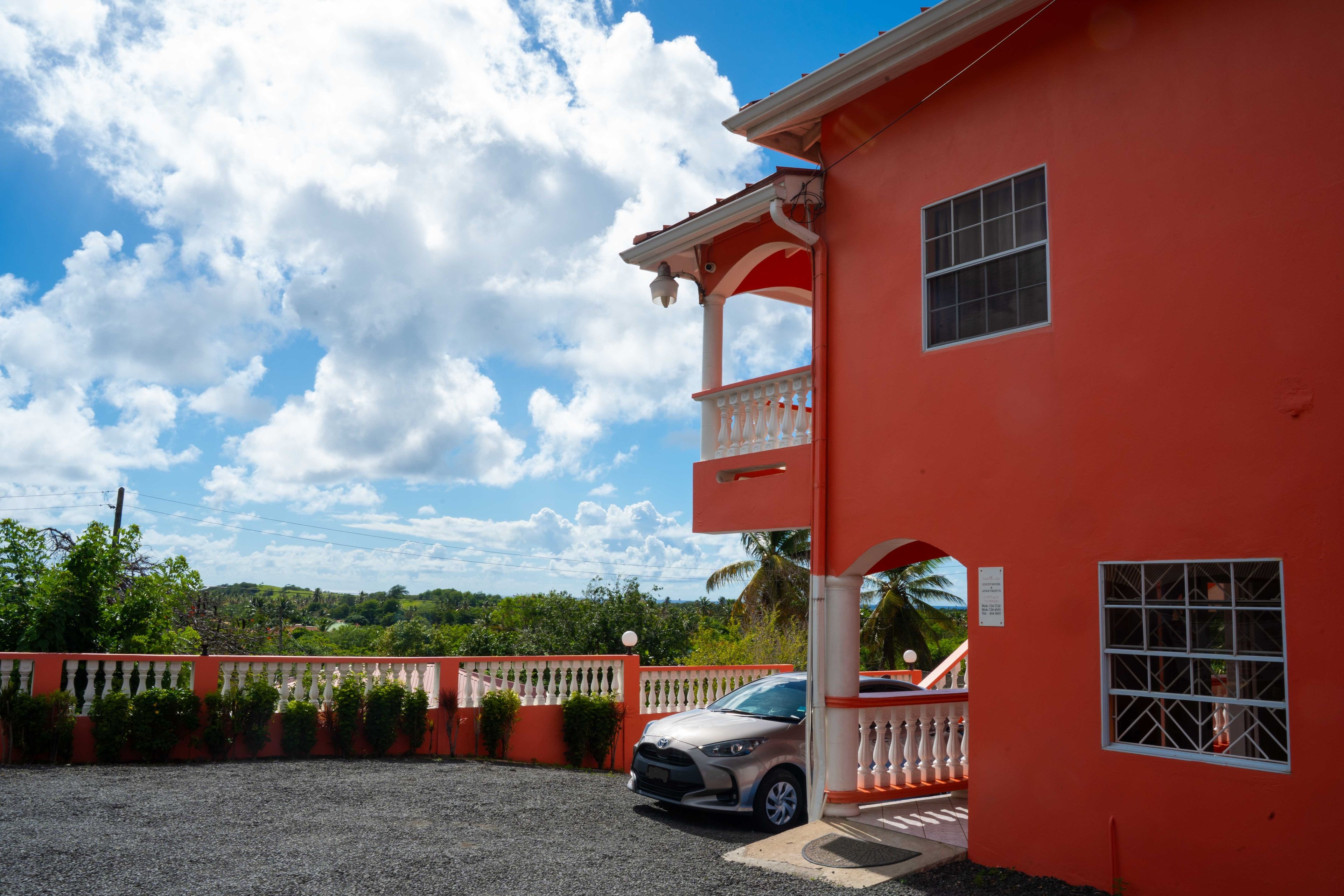 Un bâtiment rouge avec un balcon, une voiture garée devant et un ciel dégagé.