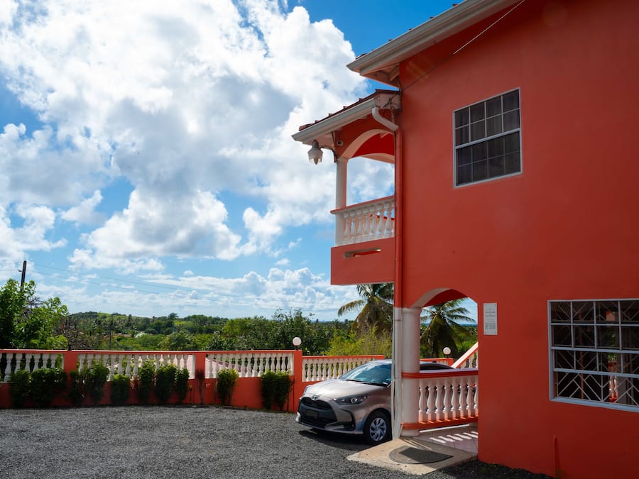 A red building with a balcony, a car parked in front, and a clear sky.