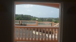 Een balkon met een witte balustrade en uitzicht op een groen landschap met bomen en een heldere lucht.