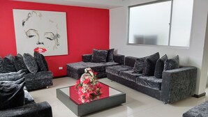 A modern living room with a red accent wall, a large abstract painting, and a decorative centerpiece on a glass coffee table. - Europa Hotel Boutique (Manizales)