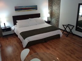 Una habitación de hotel con una cama, una mesita de noche, una lámpara, una pequeña mesa y un cuadro en la pared.