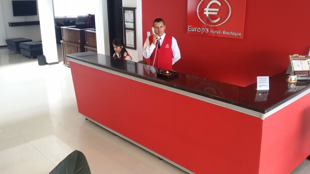 A reception desk with a red color scheme, a logo on the wall, and a sign indicating payment acceptance. - Europa Hotel Boutique (Manizales)