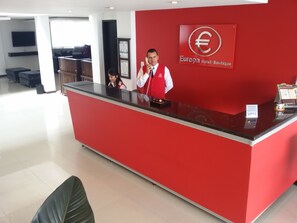 Ein Empfangsschalter mit roter Farbgestaltung, ein Logo an der Wand und ein Schild, das die Zahlungsannahme kennzeichnet.
