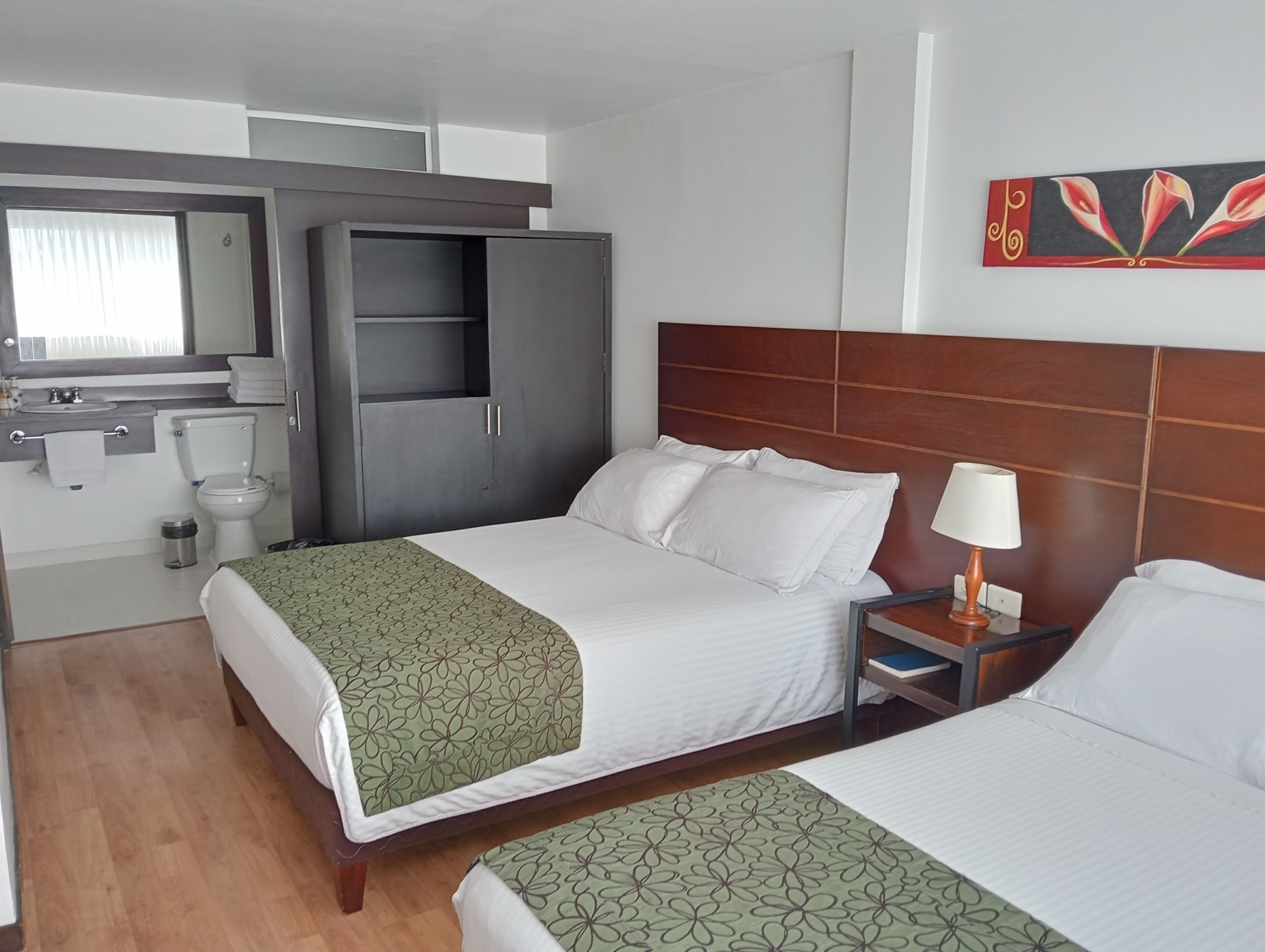A hotel room with a bed, a nightstand, a mirror, a wardrobe, and a bathroom.