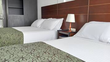 Habitación de hotel con dos camas, un armario, una mesita de noche con lámpara y un cuadro colgado en la pared.