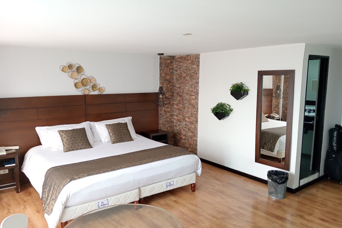 Ein modernes Hotelzimmer mit einem großen Bett, einem runden Glastisch, einem kleinen weißen Stuhl, einem Spiegel und zwei Wandpflanzgefäßen.