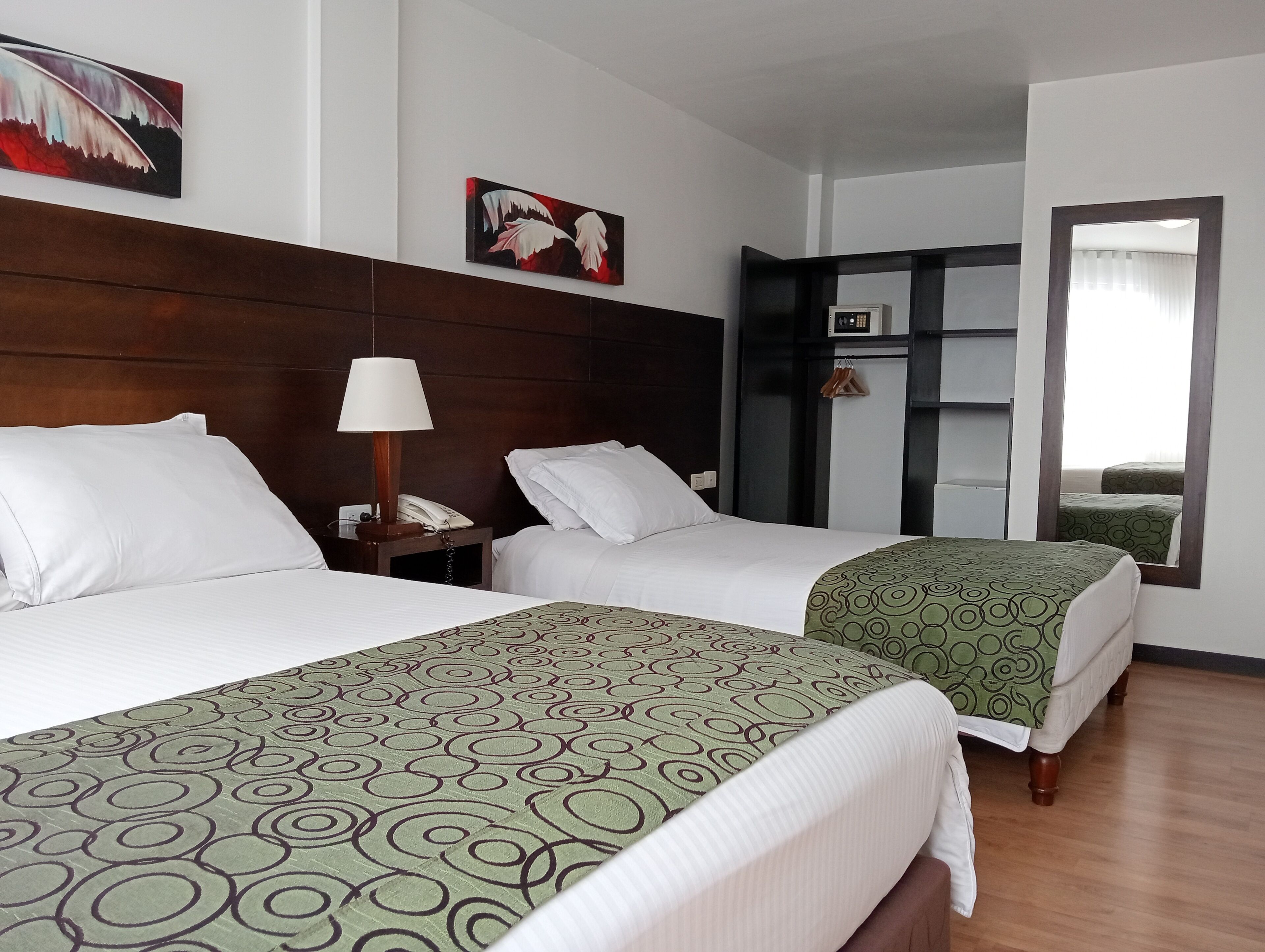 A hotel room with two beds, a bedside table with a lamp, a telephone, a wardrobe, and a mirror.