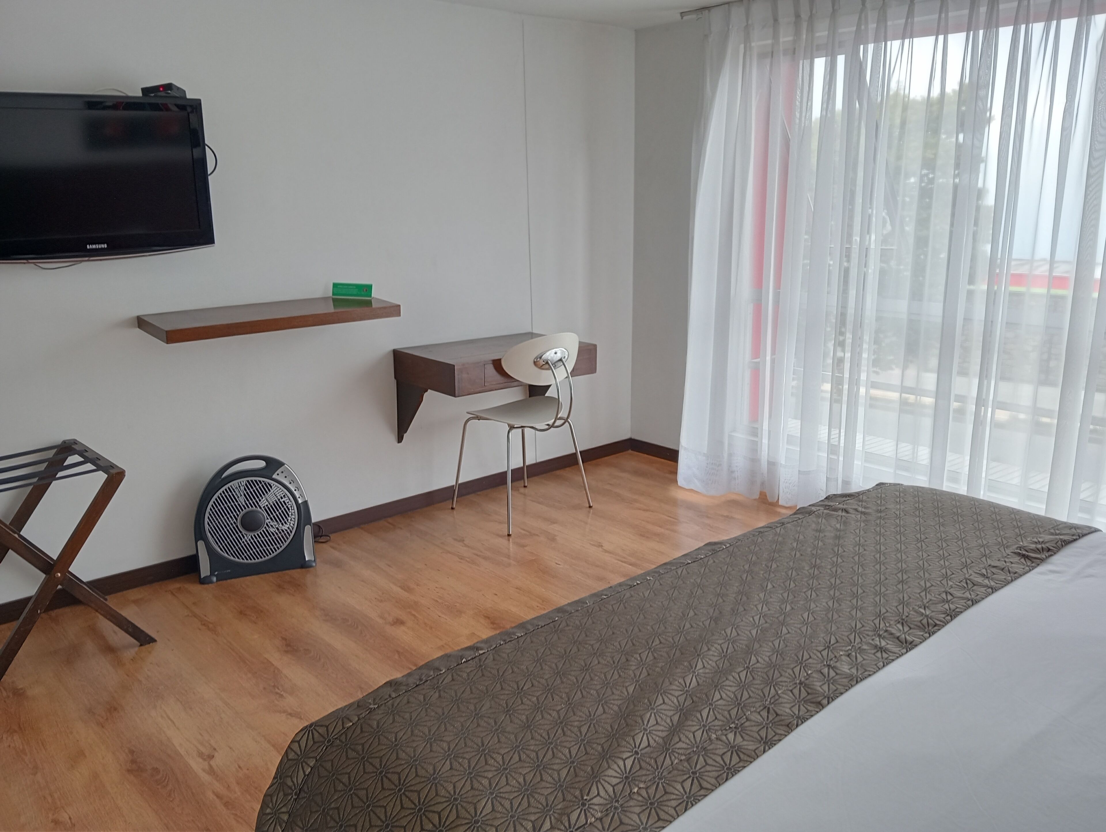 Habitación de hotel con cama, escritorio, silla, televisión y ventana con cortinas.