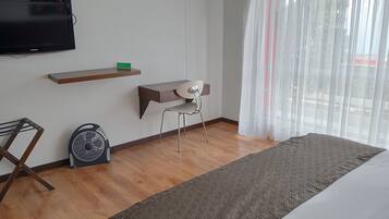 Habitación de hotel con cama, escritorio, silla, televisión y ventana con cortinas.