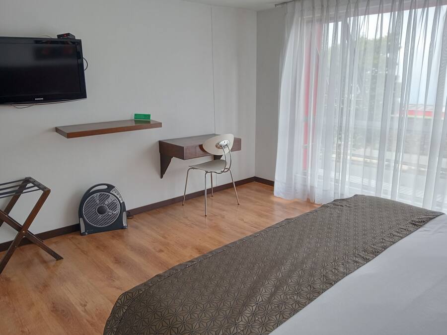 Habitación de hotel con cama, escritorio, silla, televisión y ventana con cortinas.