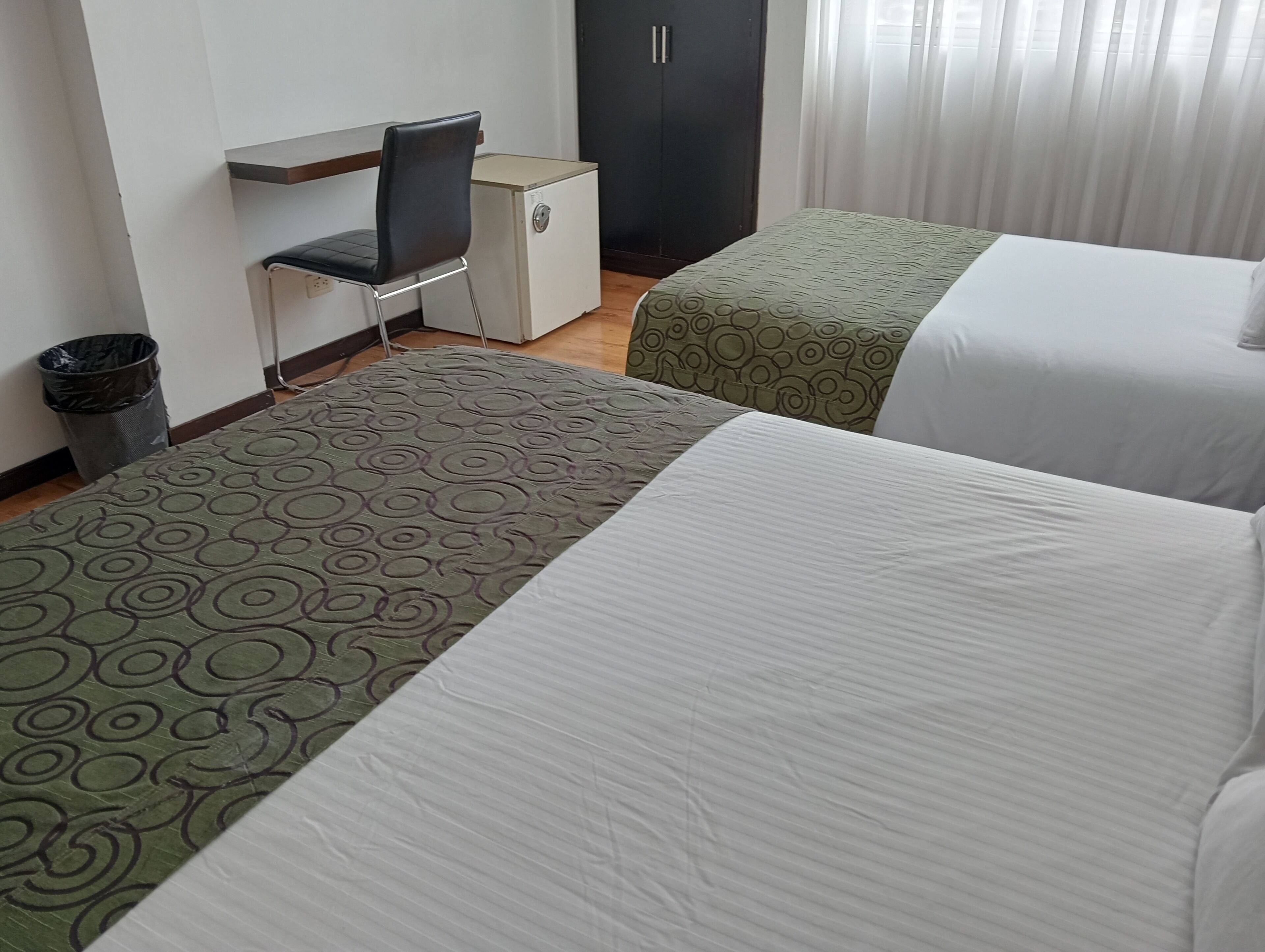 Habitación de hotel con dos camas, un escritorio, una silla, un armario y un cesto de basura.