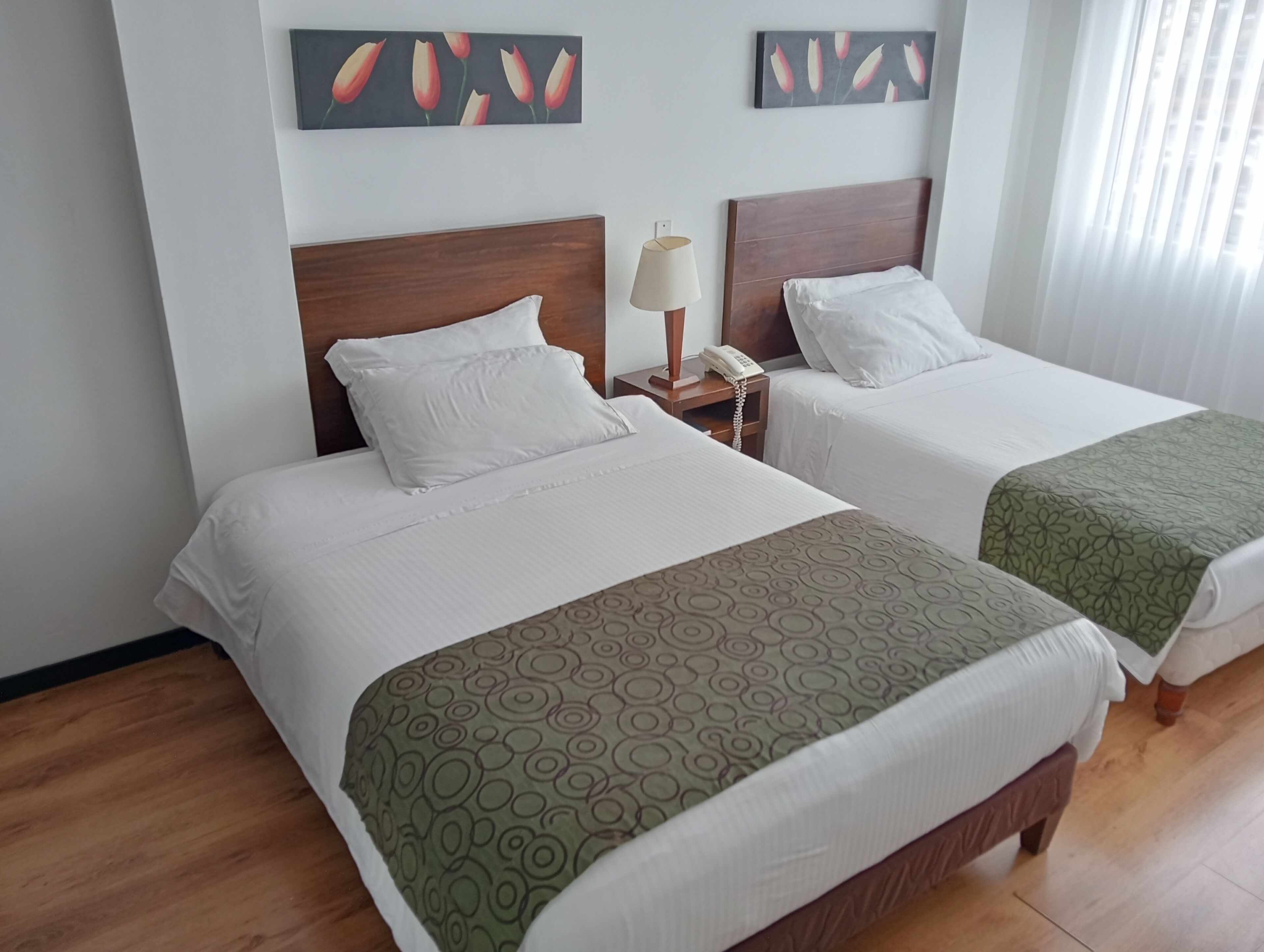 Deux lits simples avec des têtes de lit en bois, du linge de lit blanc, une table de chevet avec une lampe et un téléphone.