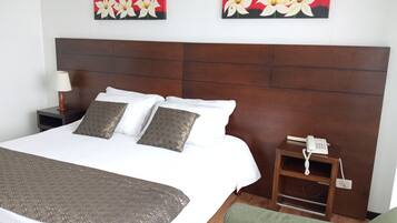 A hotel room with a large bed, two pillows, a bedside table with a lamp, a phone, and two wall-mounted paintings.
