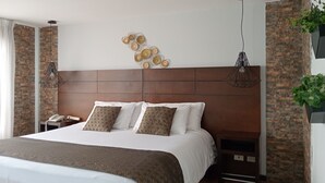A modern bedroom with a large bed, a wooden headboard, decorative wall art, and a hanging light fixture. - Europa Hotel Boutique (Manizales)