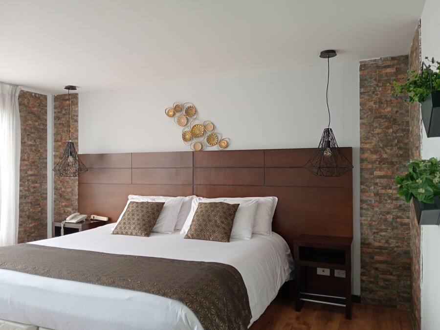 Un dormitorio moderno con una cama grande, cabecera de madera, detalles decorativos en la pared y una lámpara colgante.