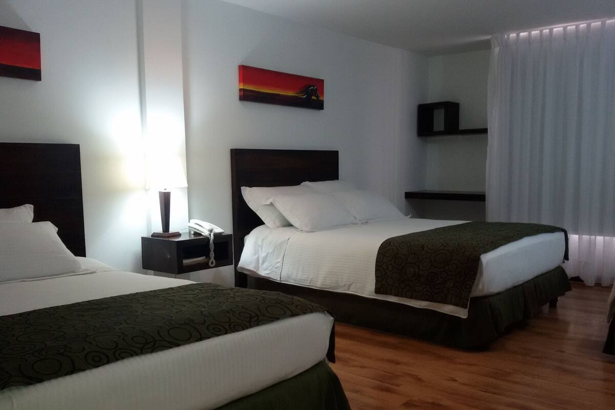 Ein Hotelzimmer mit zwei Betten, einem Nachttisch mit Lampe und Telefon, einem Bild an der Wand und einem Fenster mit Vorhängen.