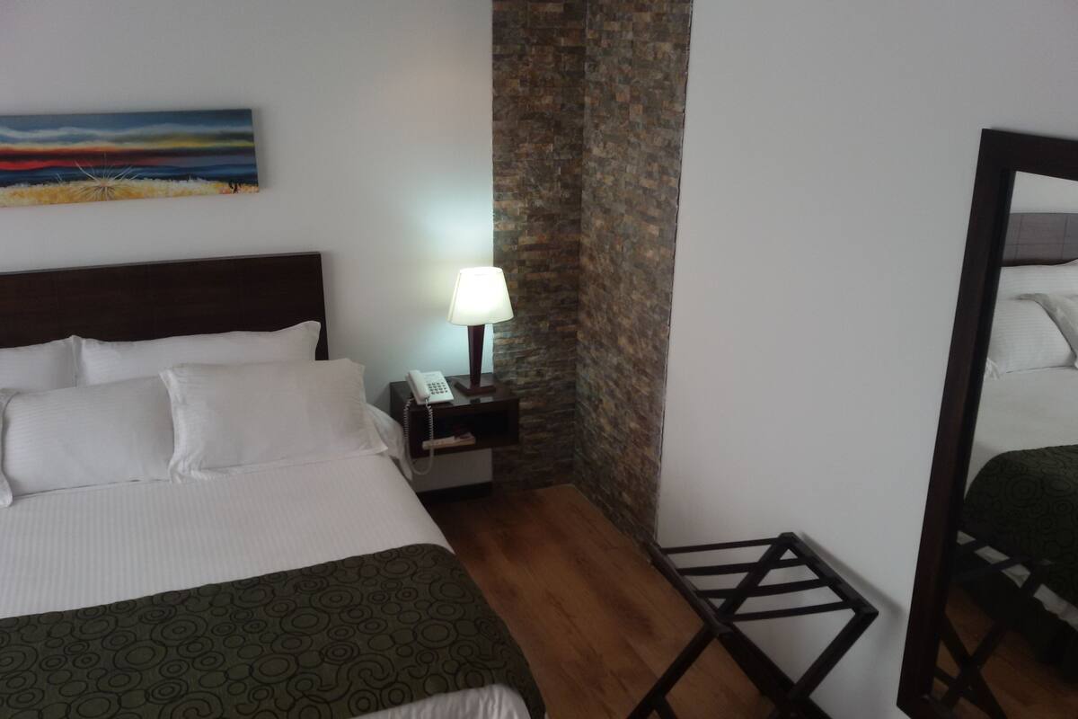 Ein Hotelzimmer mit Bett, Nachttisch mit Lampe, Spiegel und einem Bild an der Wand.