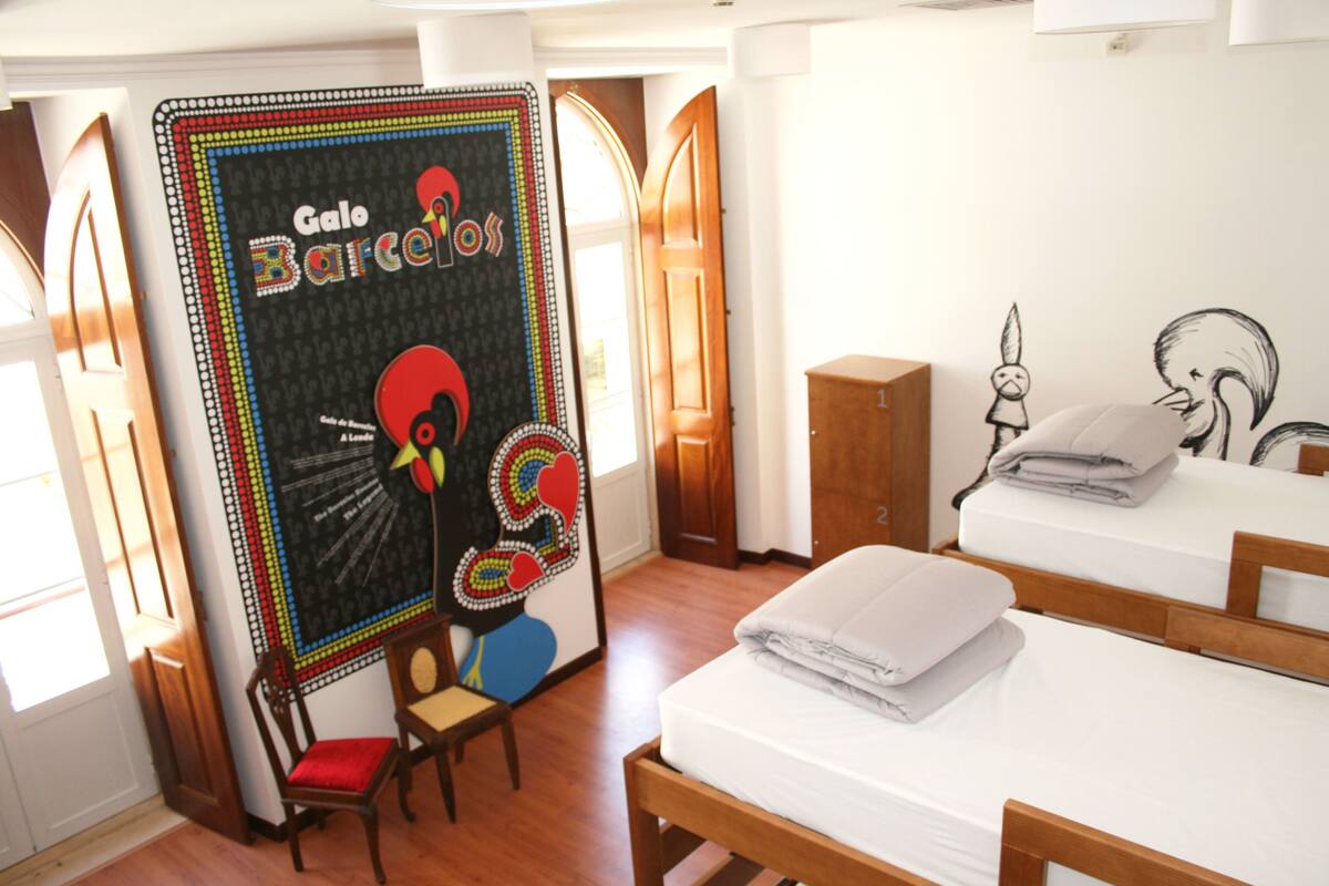 A hotel room with a bed, a chair, a wooden cabinet, and a colorful wall decoration.