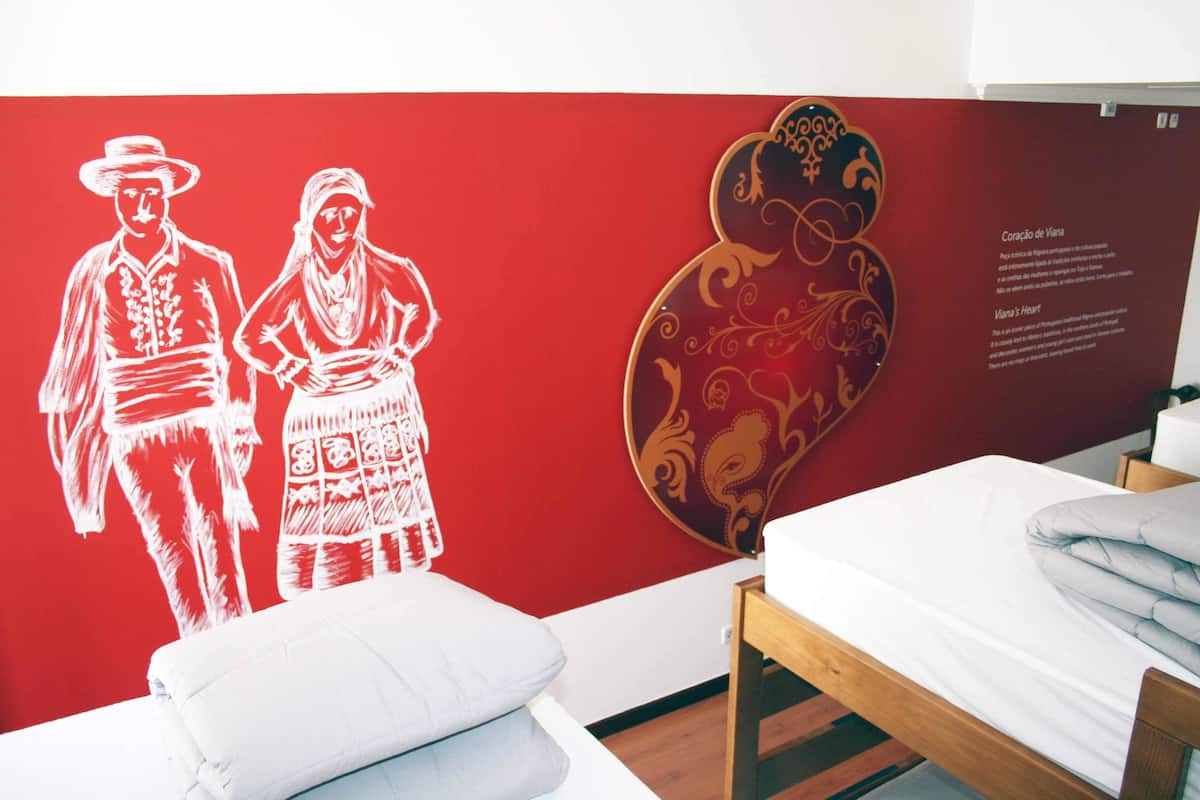 A room with a red wall, a bed with white bedding, and a wall decoration depicting two figures in traditional attire.