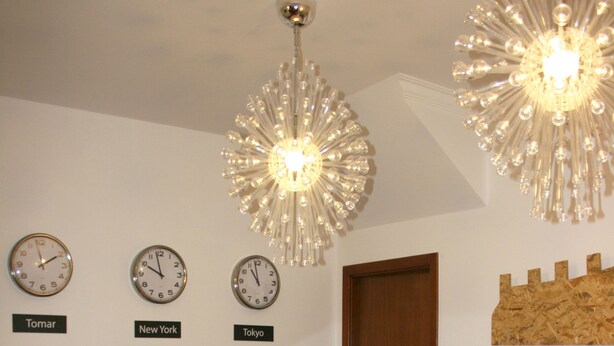 Un área de recepción con un mostrador de madera, tres relojes identificados con 'Tomar', 'Nueva York' y 'Tokio', y una decoración de pared de madera.