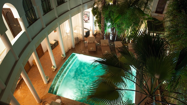 An indoor swimming pool with a view of a courtyard, surrounded by columns and palm trees. - Riad Chergui (Marrakech)