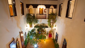A corridor with arches, a central garden, and a red carpet leading to a door. - Riad Chergui (Marrakech)