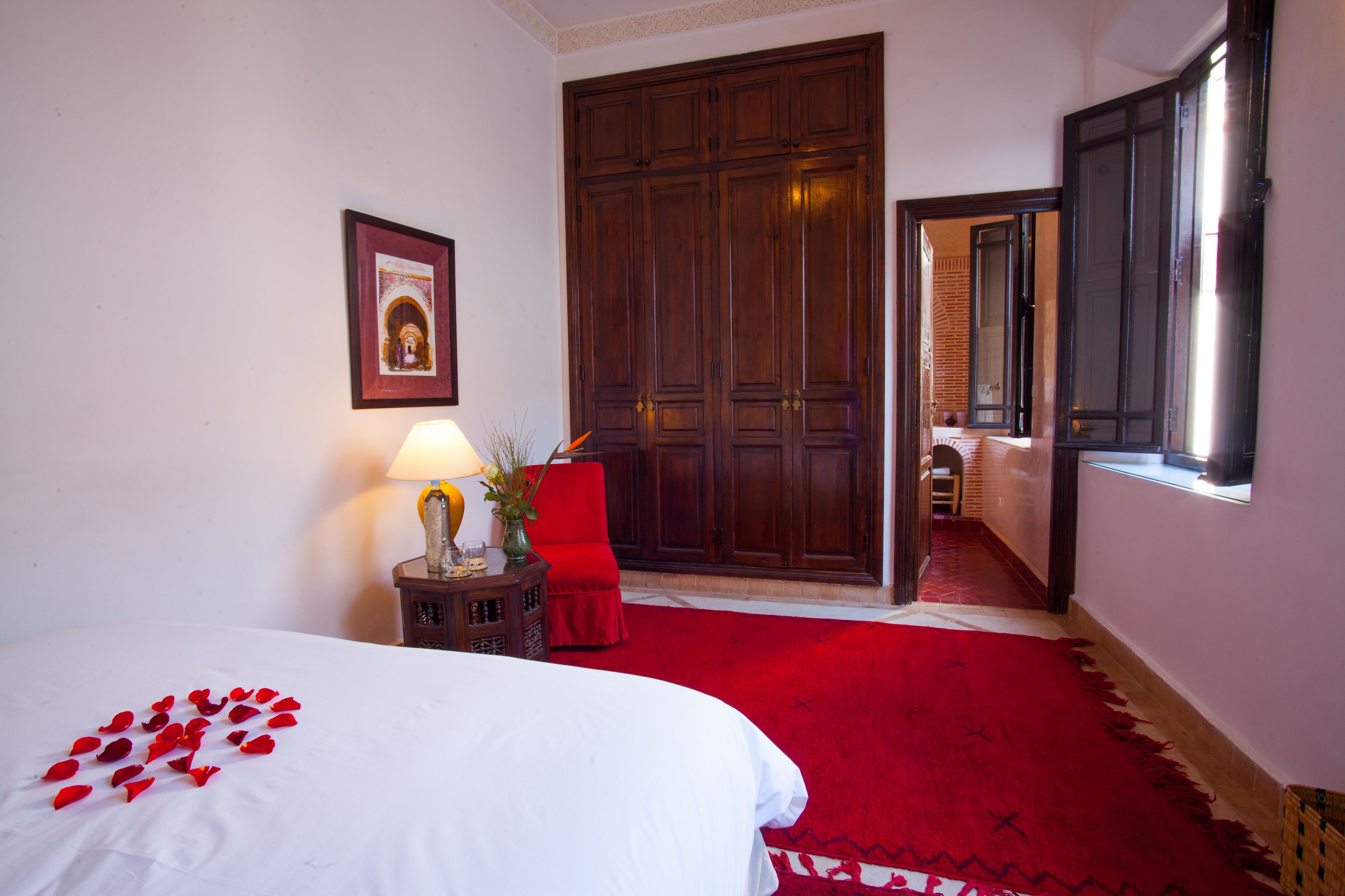 Une chambre d’hôtel avec un lit, une chaise rouge, une armoire en bois et une fenêtre.