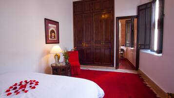 Une chambre d’hôtel avec un lit, une chaise rouge, une armoire en bois et une fenêtre.