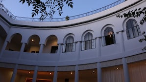 A courtyard with a white building featuring arched windows and columns, a balcony with a railing, and a hanging light fixture. - Riad Chergui (Marrakech)