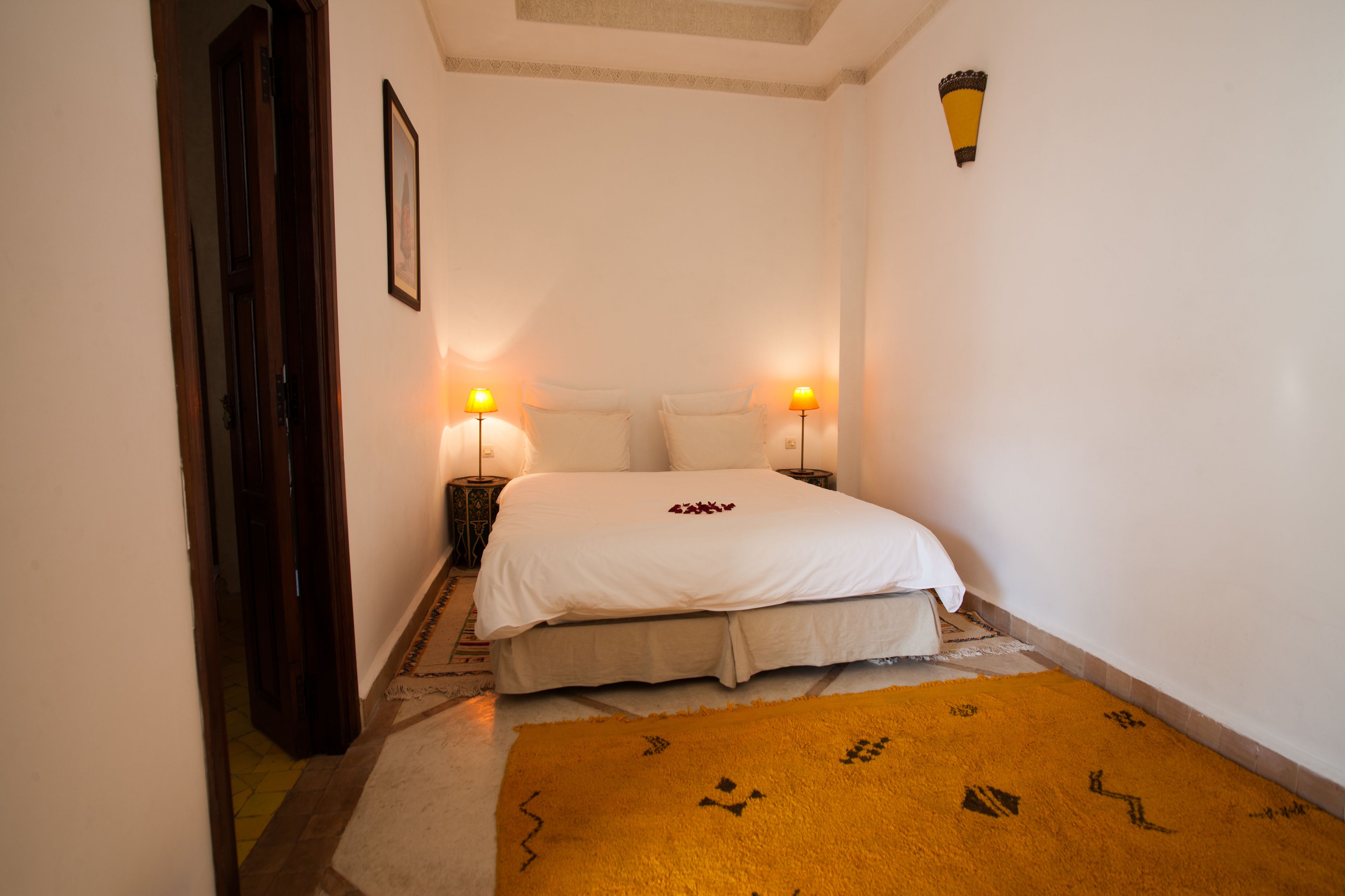 Un dormitorio con una cama, dos lámparas de noche, una alfombra y una puerta.