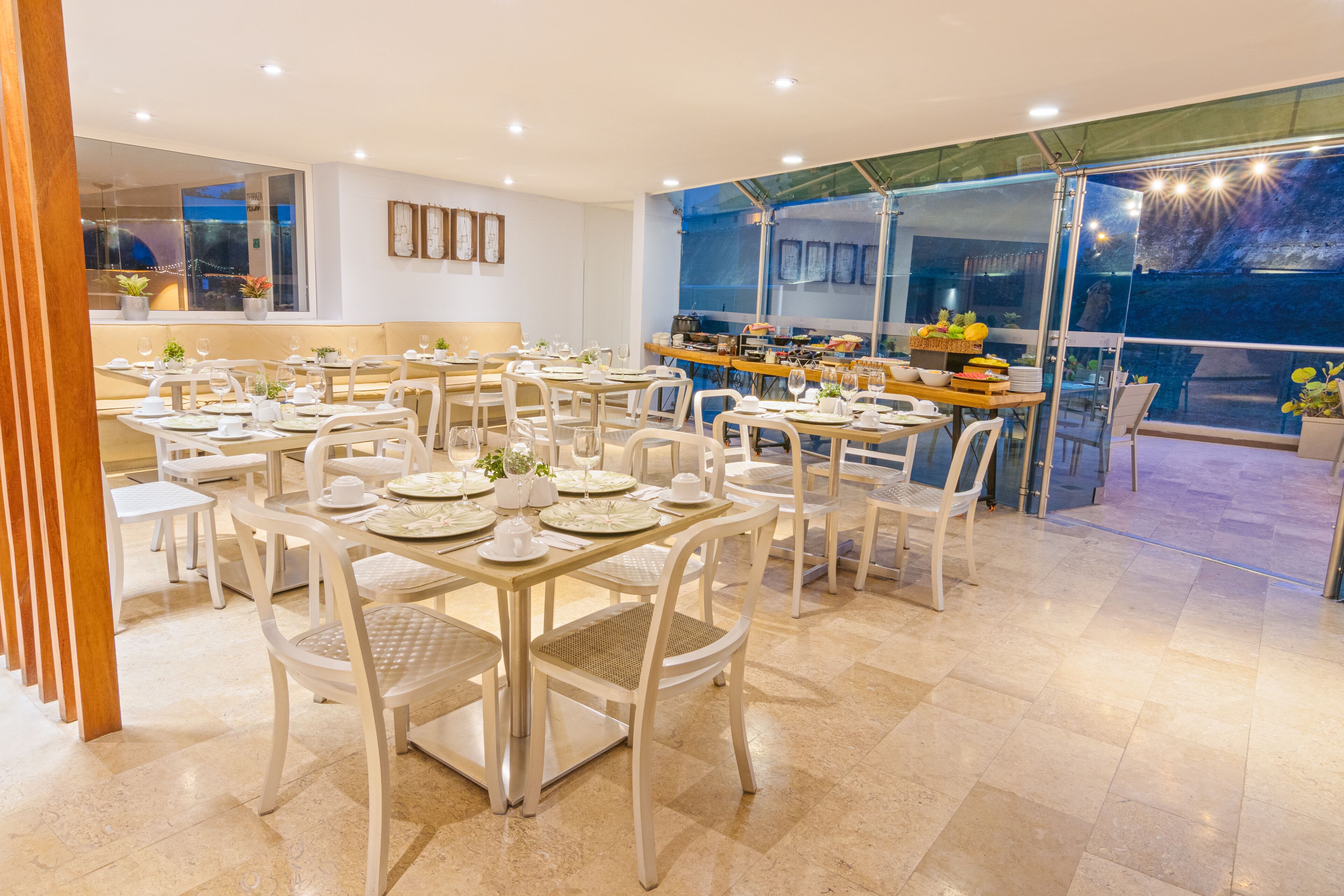 A spacious dining area with multiple tables and chairs, a kitchen counter, and large windows offering a view of the outdoors.