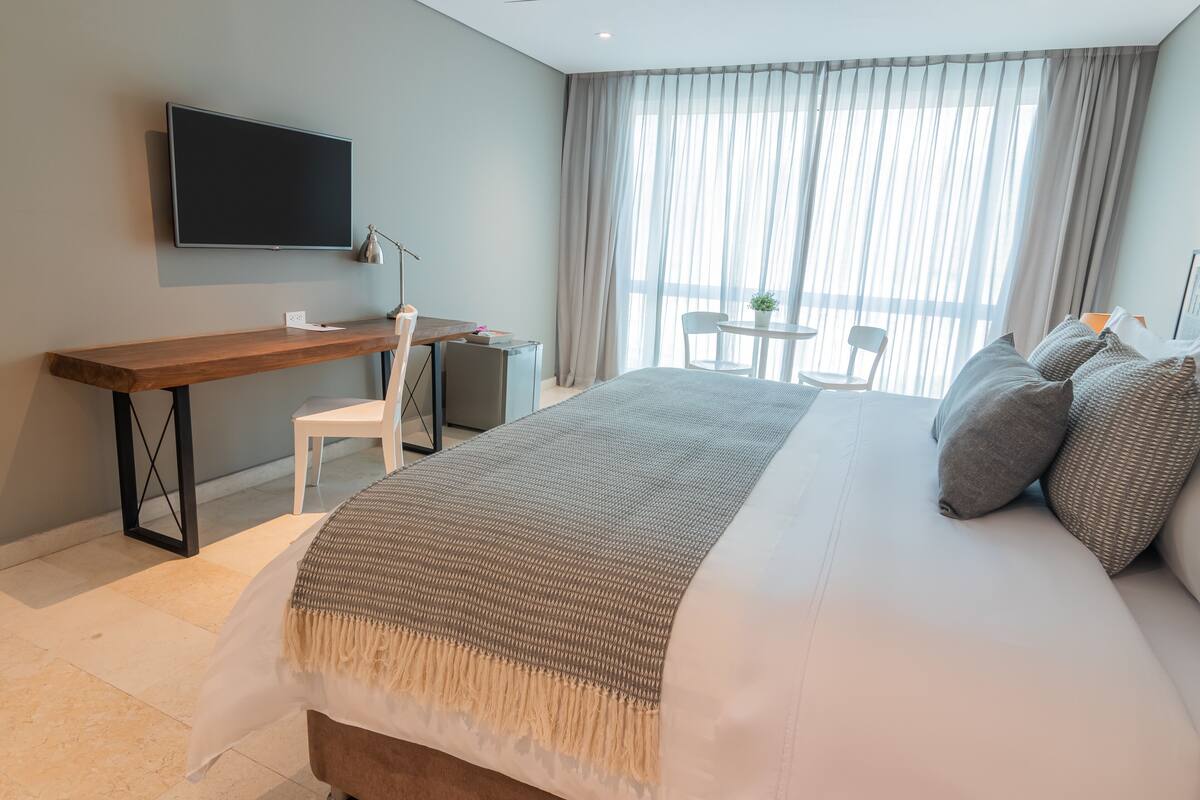 Habitación de hotel moderna con una cama grande, un escritorio, una silla, una mesita y un televisor montado en la pared.