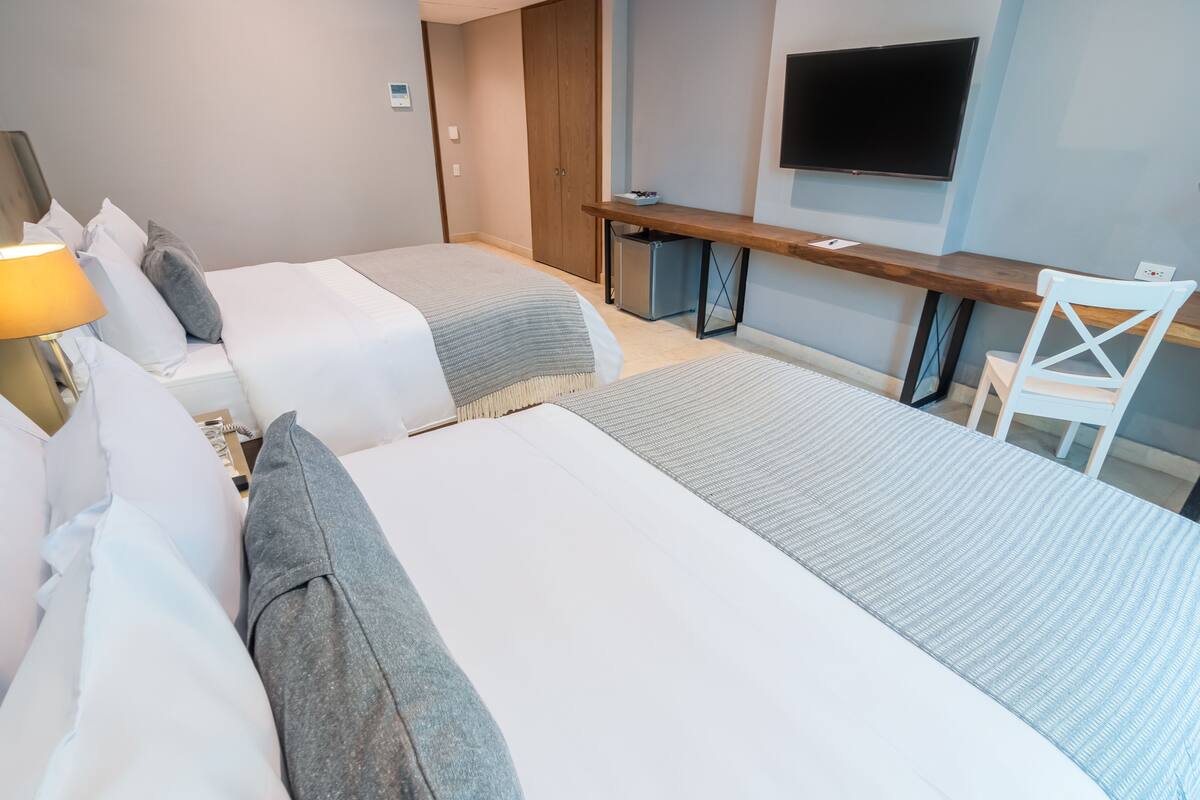 Habitación de hotel con dos camas, un escritorio, una silla, un televisor y un refrigerador pequeño.