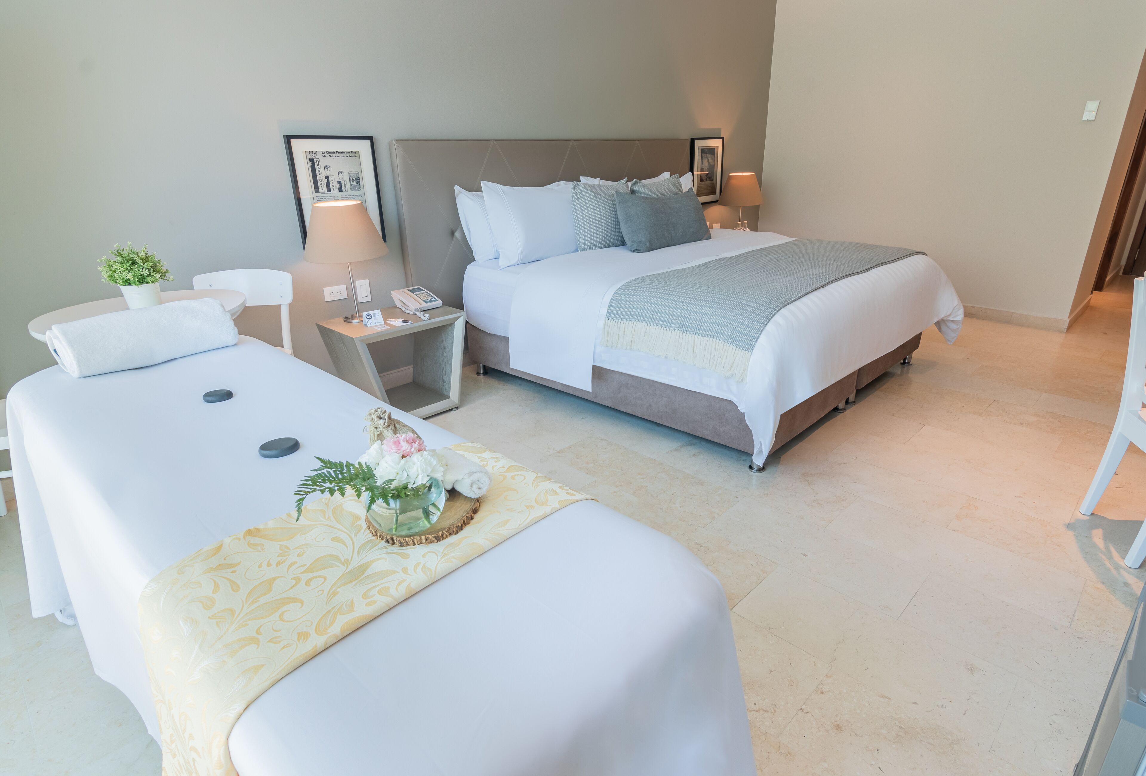 Habitación de hotel con dos camas, una mesita de noche con lámpara, una planta pequeña y una bandeja decorativa con flores.