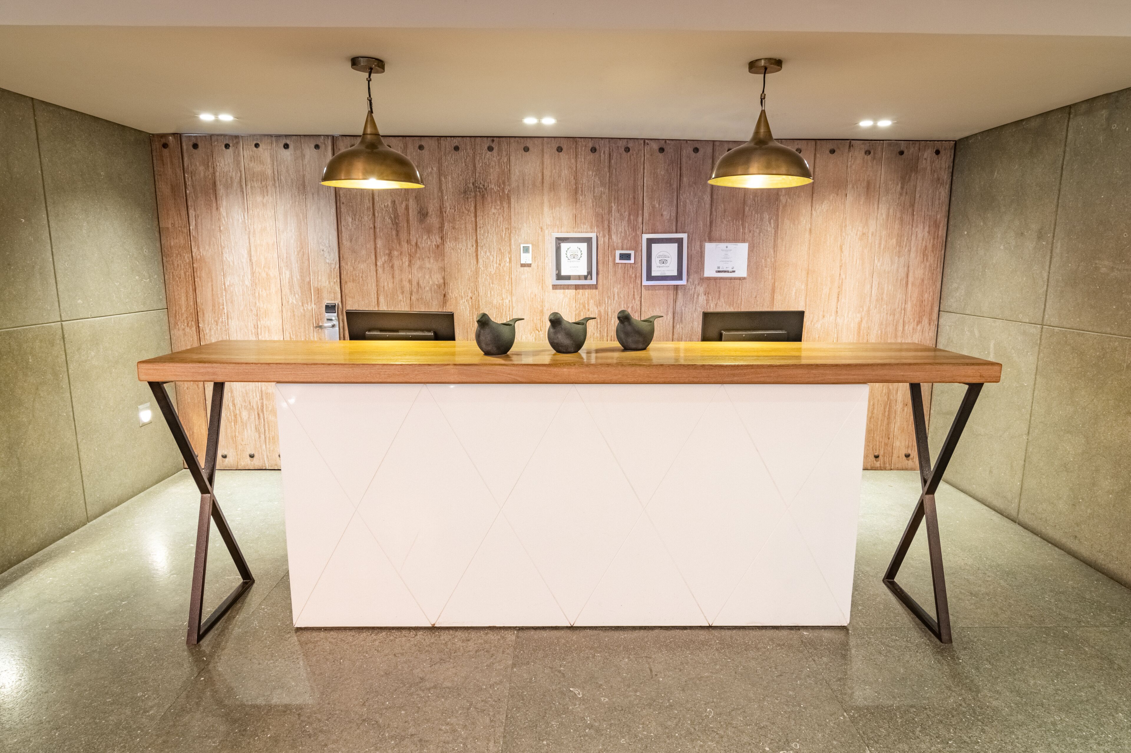 A reception desk with a wooden top and metal legs, flanked by two pendant lights.