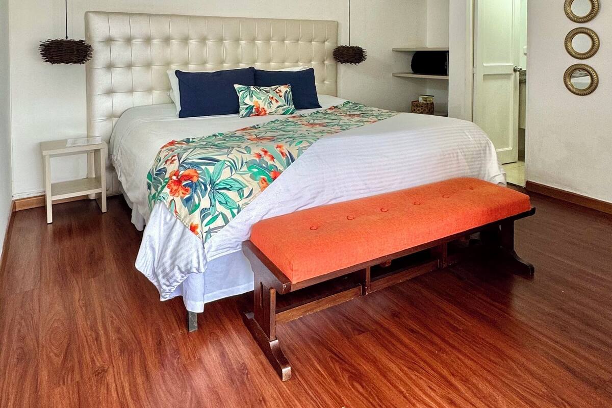 A bedroom with a large bed, a wooden bench, a white headboard, and a wooden floor.