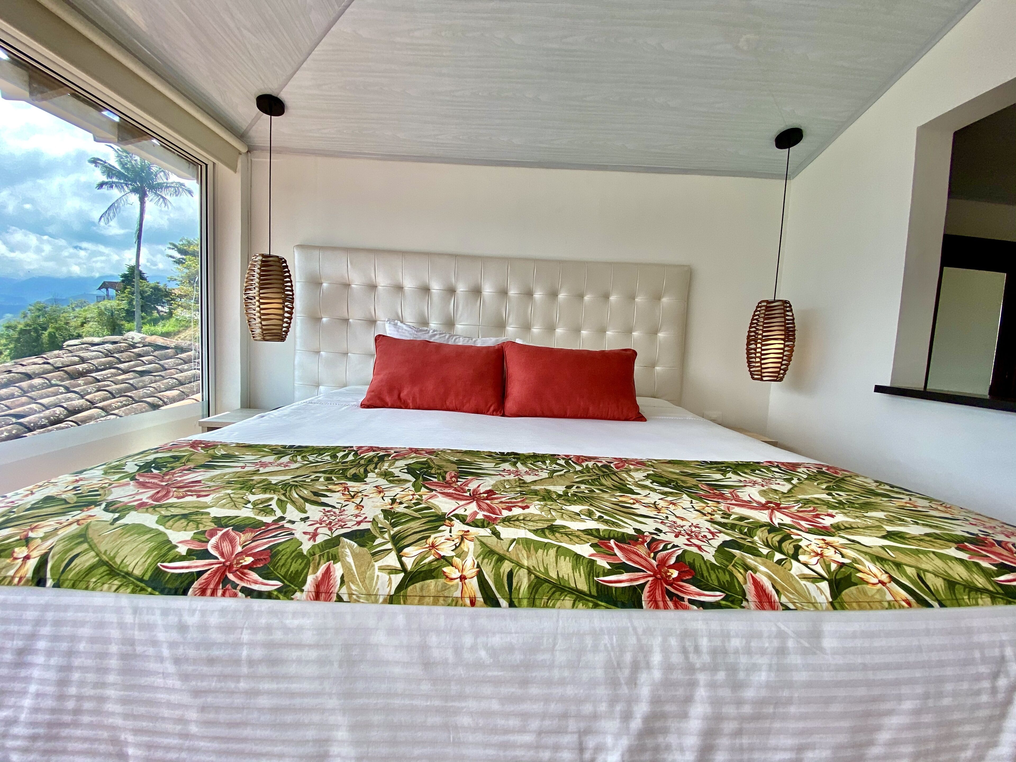 A bedroom with a large bed, a white headboard, and a view of the mountains through the window.