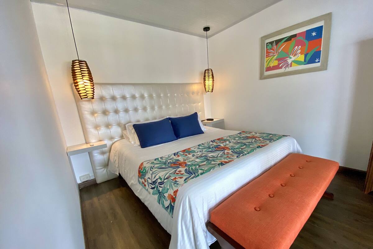 A bedroom with a tufted headboard, a floral bedspread, two bedside tables, and a bench.