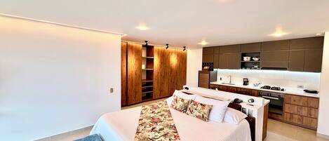 A modern bedroom with a large bed, a wardrobe, and a kitchenette.
