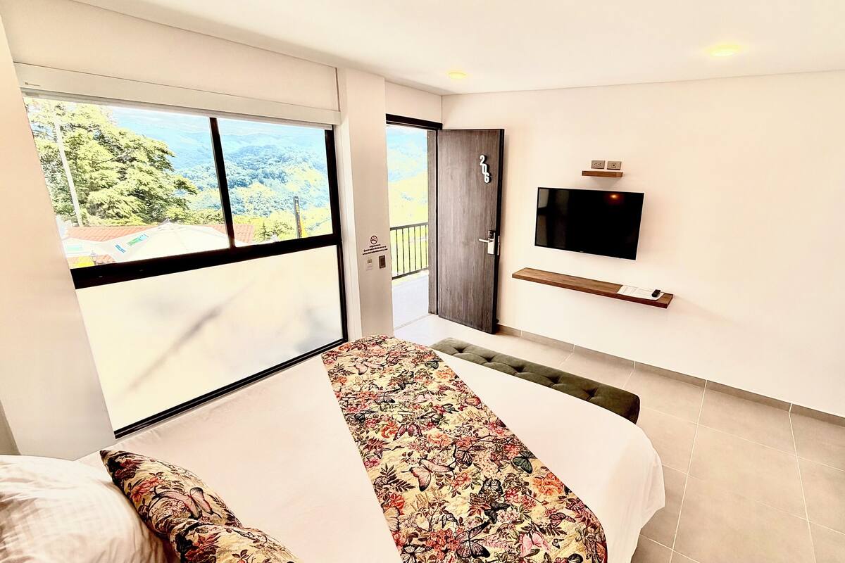 A hotel room with a bed, a TV, a balcony, and a door leading outside.