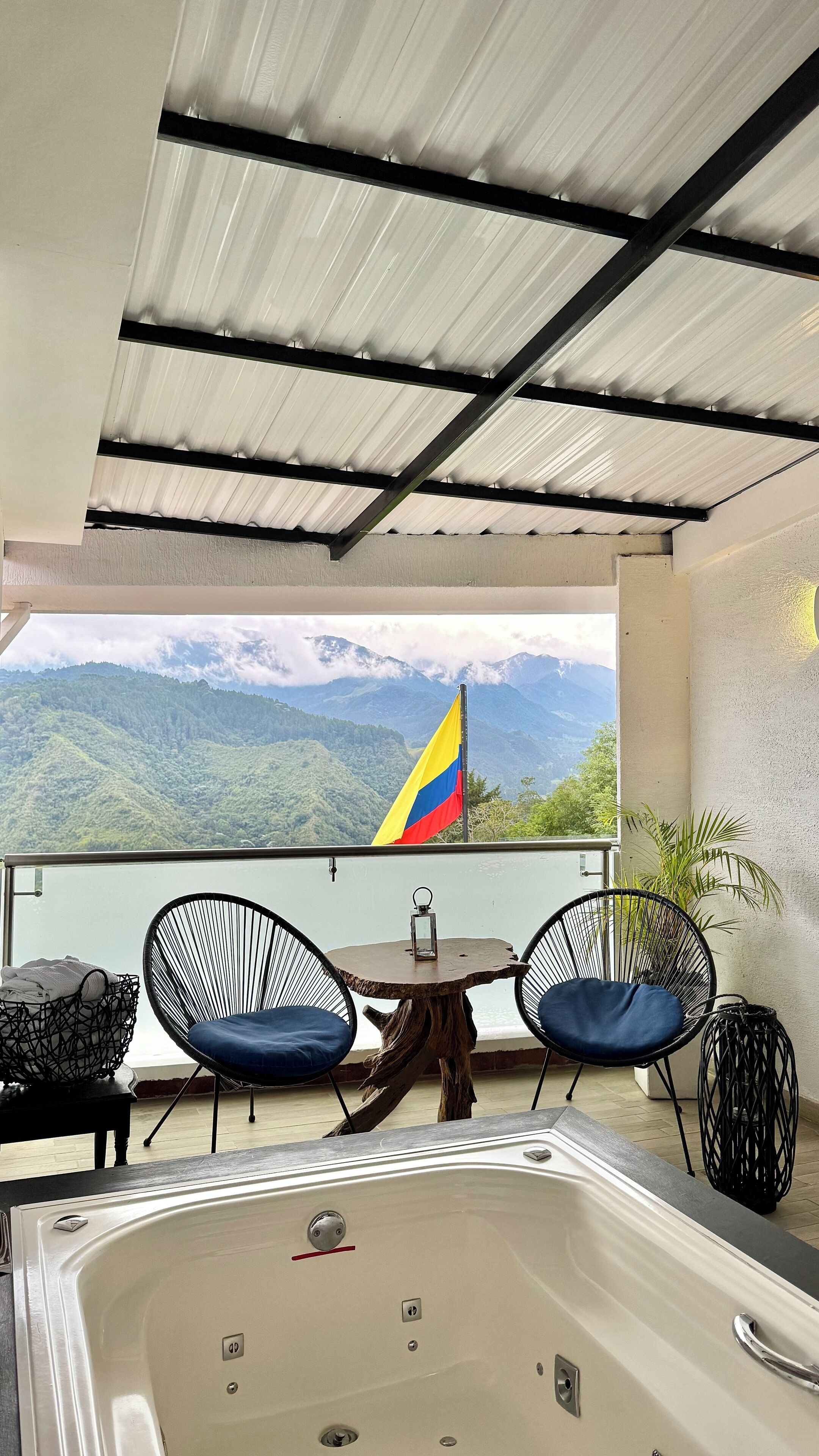 A balcony with a view of mountains, a flag, and a hot tub.