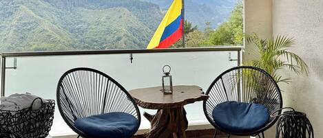A balcony with a view of mountains, a flag, and a hot tub.