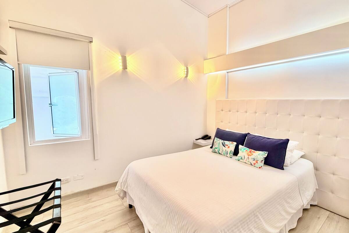 A hotel room with a bed, a nightstand, a chair, and a window with blinds.