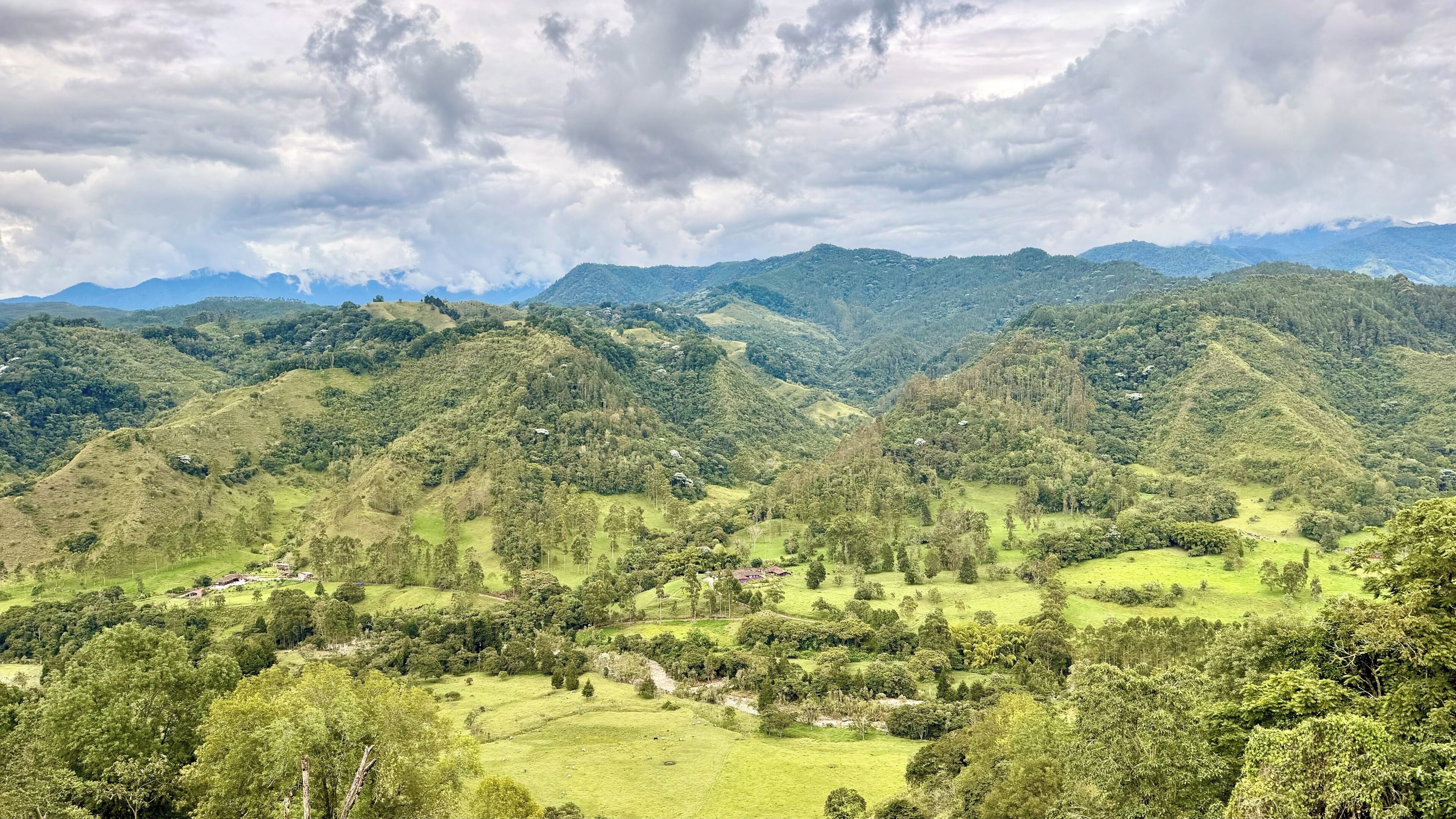 A mountainous landscape with rolling hills, scattered trees, and a few small buildings.