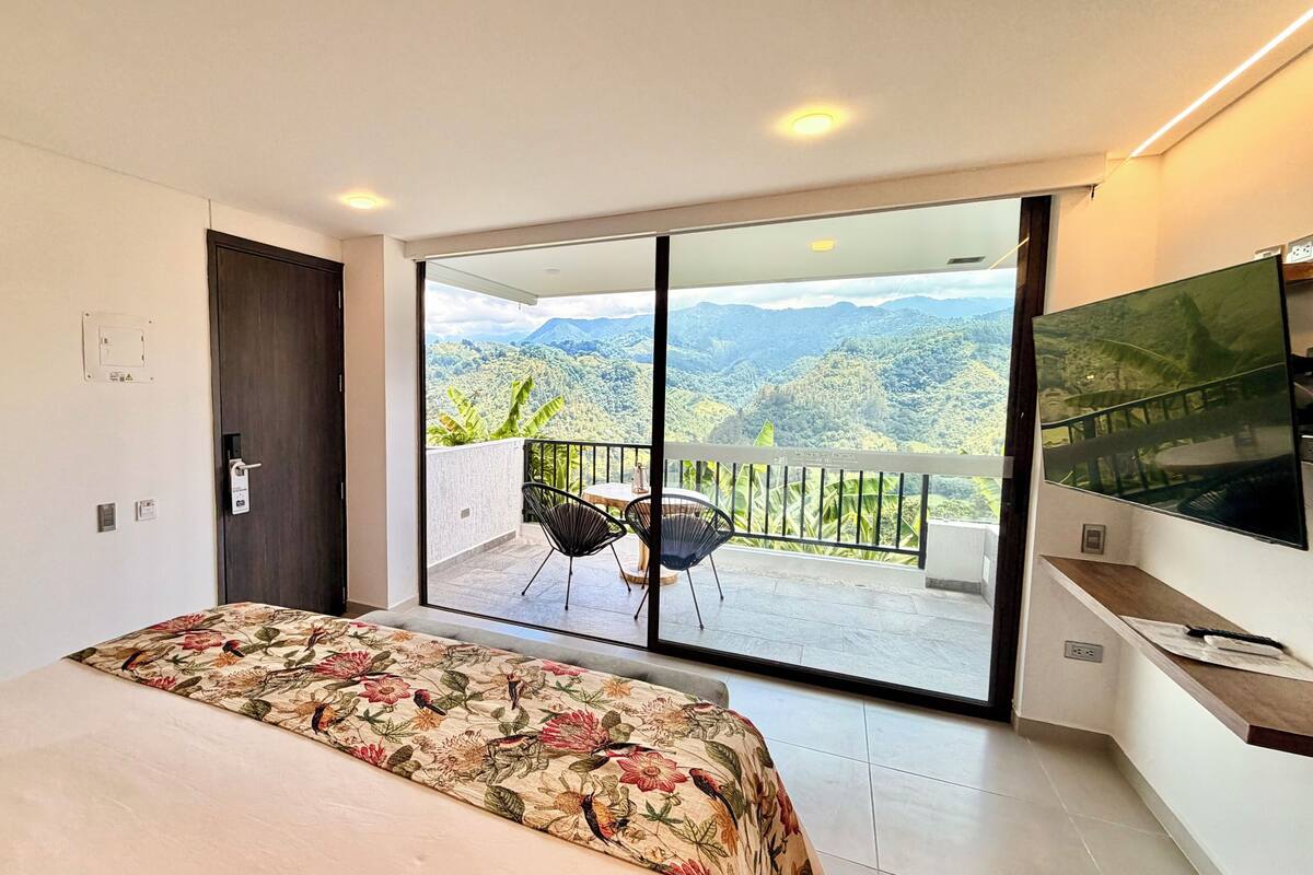 A bedroom with a bed, a sliding glass door to a balcony, a TV, and a small table.