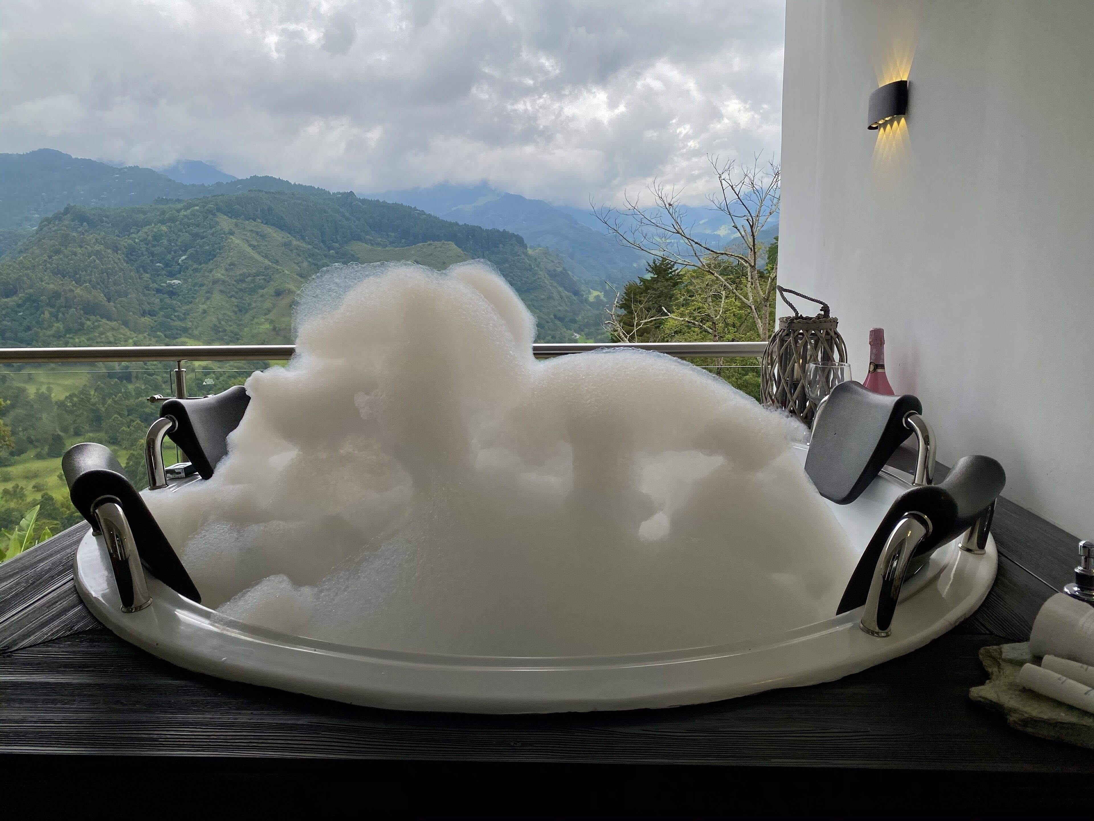 A bathtub filled with bubbles, a wooden table, a bottle, and a wicker basket.
