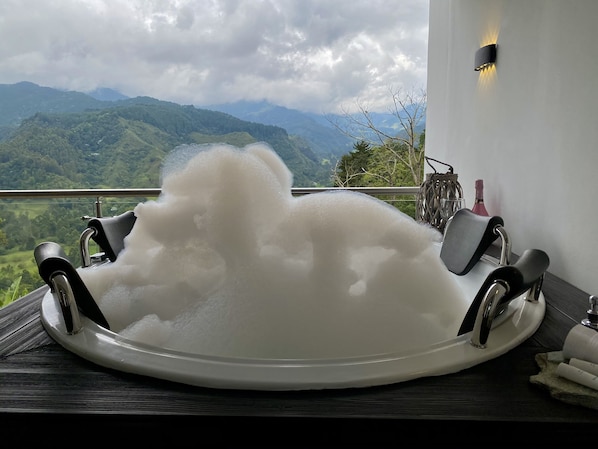 Une baignoire remplie de mousse, une table en bois, une bouteille et un panier en osier.